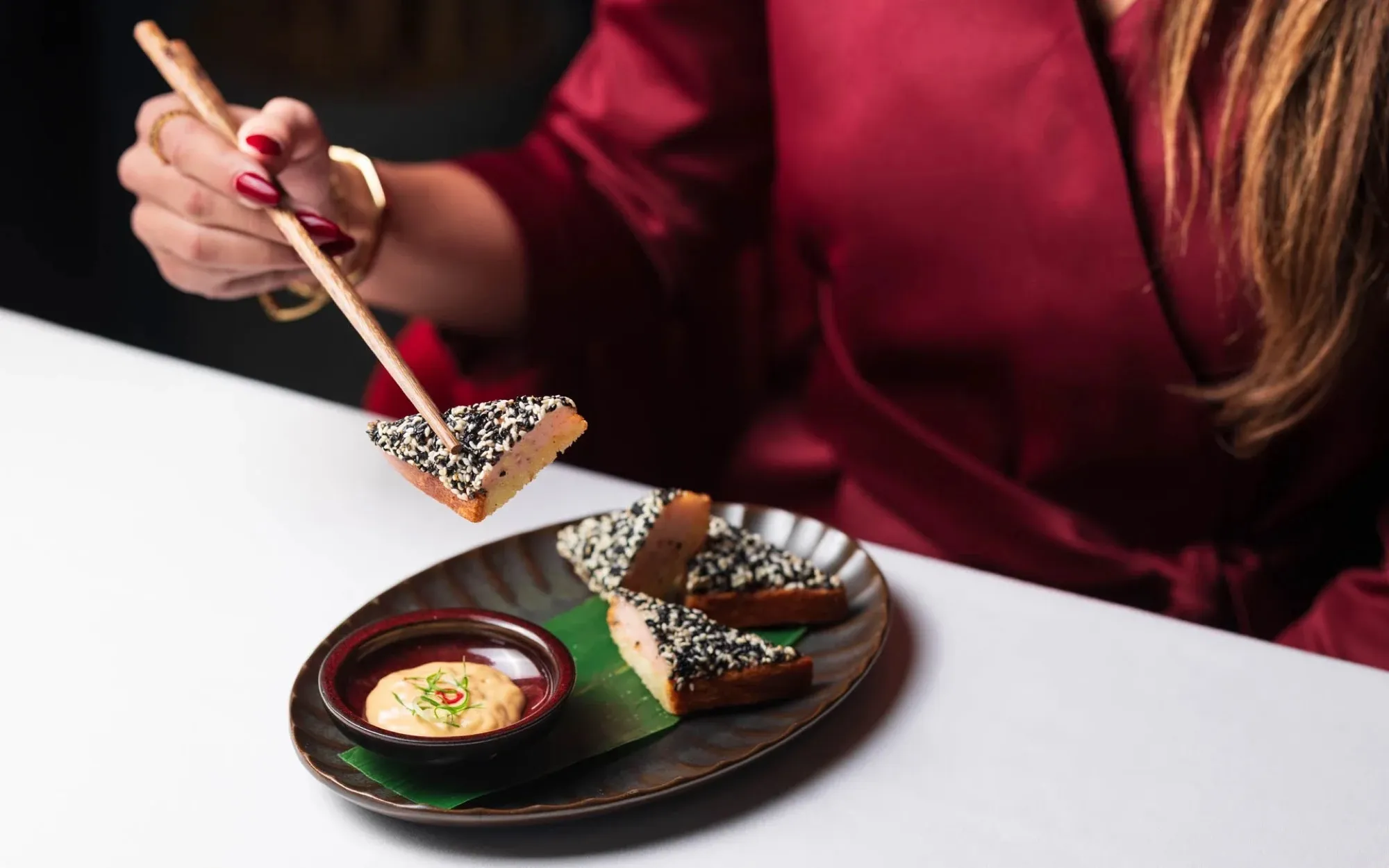 Chopsticks lifting a dessert from a dark plate